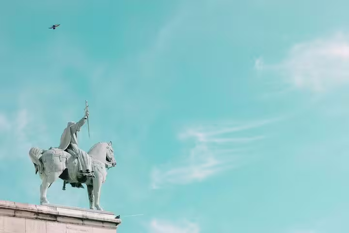 Equestrian statue of a knight raising a sword atop a stone pediment in Paris against a turquoise sky