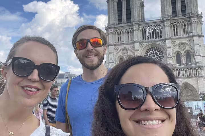 Three smiling tourists taking a selfie in front of Notre-Dame Cathedral in Paris on a sunny day