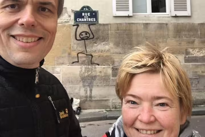 Two smiling tourists taking a selfie on Rue des Chantres in Paris with street art graffiti on wall behind them