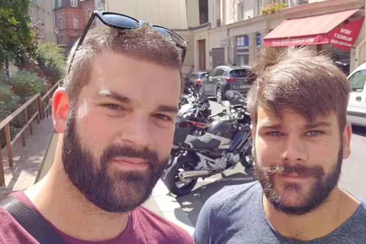 Two bearded men taking a selfie on a Paris street with motorcycles and buildings in background