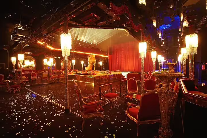 Glamorous Parisian cabaret venue with red velvet chairs, ornate gold decor, and a draped stage lit in warm golden light