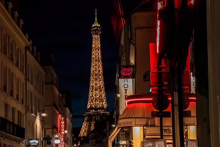 Eiffel Tower illuminated at night viewed from a Parisian street with glowing neon signs