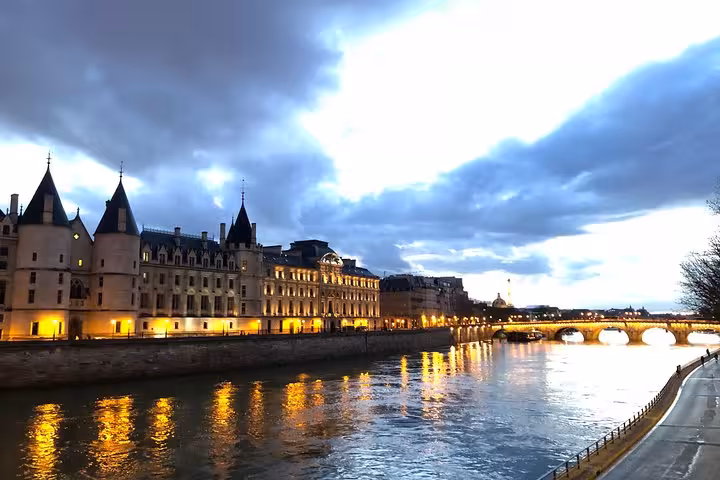 Illuminated Seine River banks at dusk with the Conciergerie castle and Pont Neuf bridge in Paris