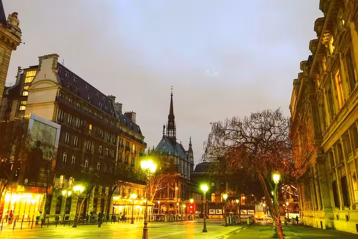 Illuminated Paris square at night with Gothic church spire and glowing street lamps on empty cobblestone streets