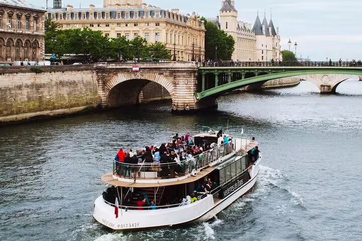 Scenic river cruise boat on the Seine River passing under a bridge with historic Paris buildings in background