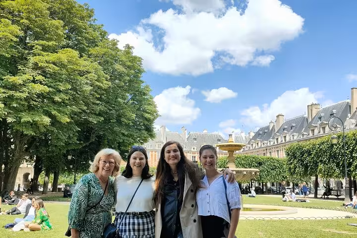 Four women smiling together at Place des Vosges park in Paris on a sunny day