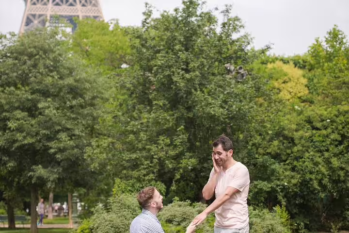 Man proposing on one knee to surprised partner in Paris park near Eiffel Tower