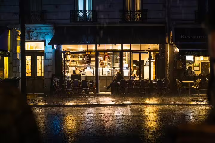 Rainy night at a warmly lit Paris restaurant with outdoor seating on a cobblestone street