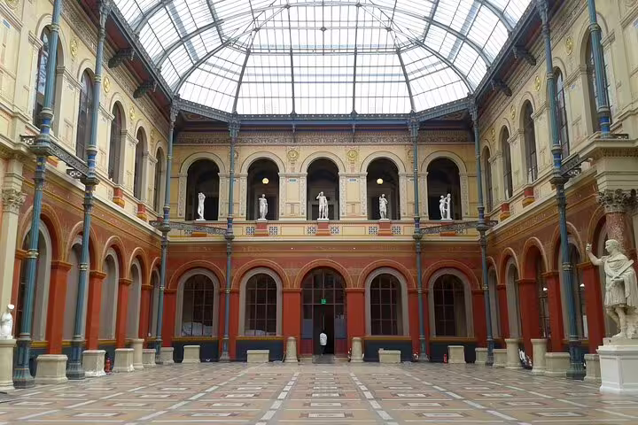 Grand neoclassical interior courtyard with glass ceiling, arched galleries, and white statues in Paris