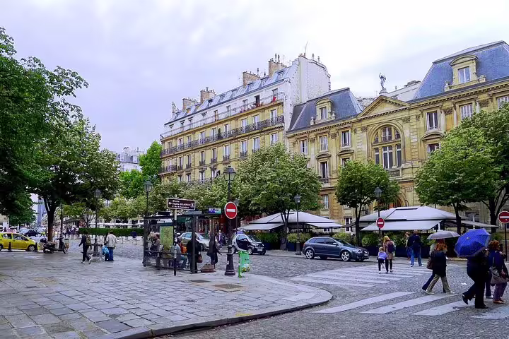 Parisian square in Saint-Germain with Haussmann buildings, trees, and pedestrians on a cloudy day