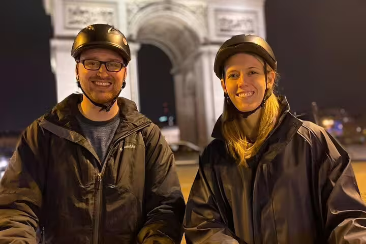 Smiling riders in helmets with Arc de Triomphe behind on Paris Segway night highlights small group tour
