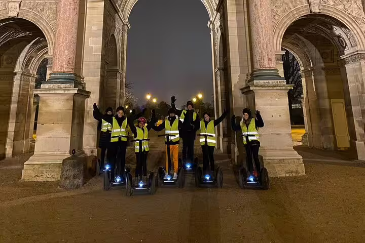 Small group on Segways at night under Paris arch monument, reflective vests on highlights tour