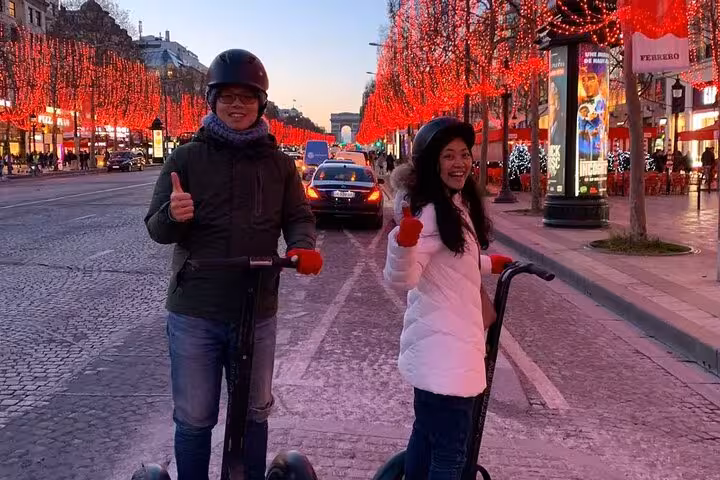 Riders on a Paris Segway night highlights small group tour on Champs-Élysées with festive lights at dusk