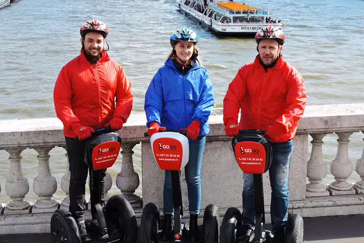 Paris Segway tour group by the Seine River with cruise boat behind, helmets on, ready for river cruise