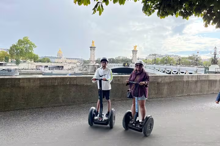 Two riders on a Paris Segway tour by the Seine near Pont Alexandre III, with Seine River cruise ticket included