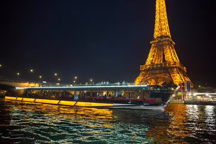 Illuminated Seine River cruise boat passing the glowing Eiffel Tower at night in Paris
