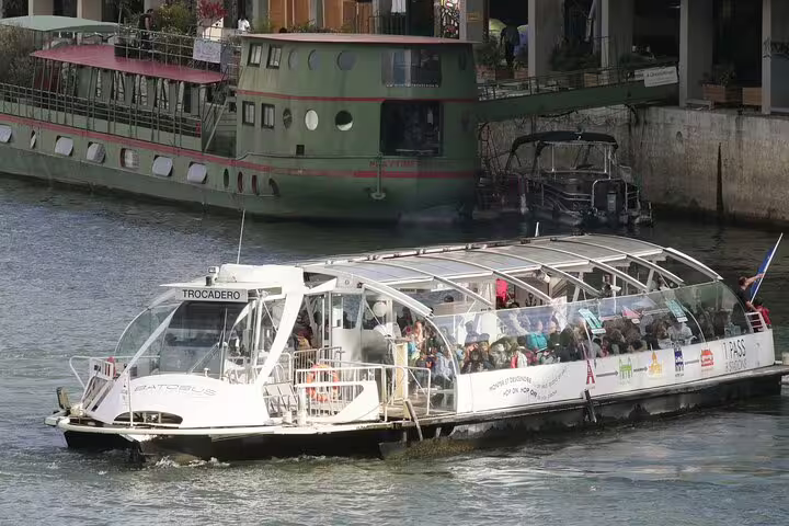 Batobus Seine river cruise boat packed with tourists passing green houseboat in Paris