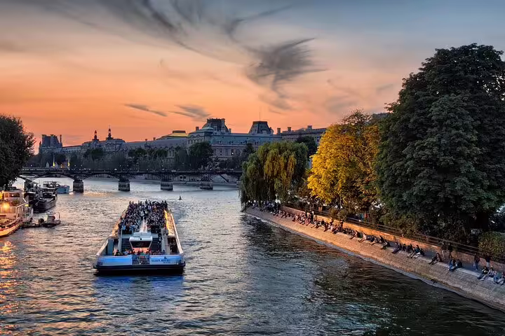 Seine River cruise boat at sunset with Paris skyline and tree-lined riverbank in background