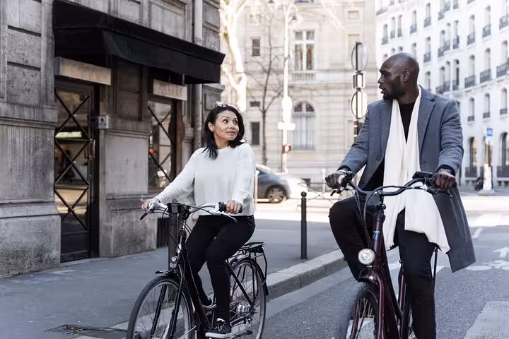 Couple cycling through central Paris streets on a Seine River bike tour, with optional Louvre Museum entry