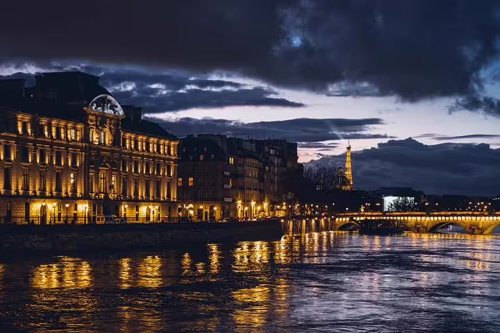 Paris skyline at night with illuminated buildings along the Seine River and Eiffel Tower in background
