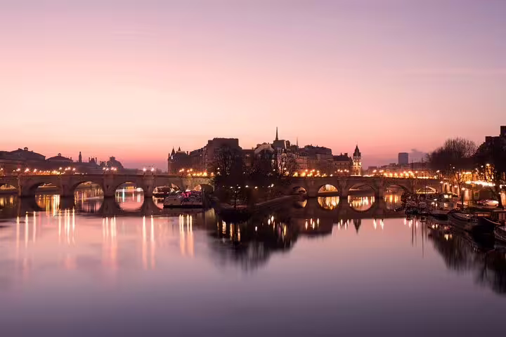 Paris Seine River at sunset with illuminated Pont Neuf bridge reflecting on calm water