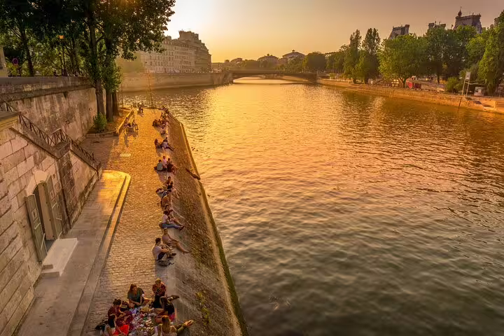 People relaxing along the Seine River at sunset in Paris, showcasing the serene atmosphere of the Highlights & Secrets private tour.