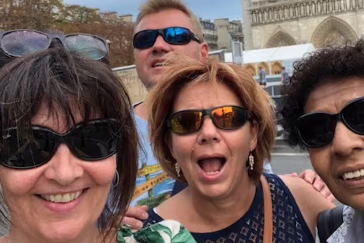 Four tourists taking a selfie near the Seine River in Paris with Notre-Dame Cathedral in background