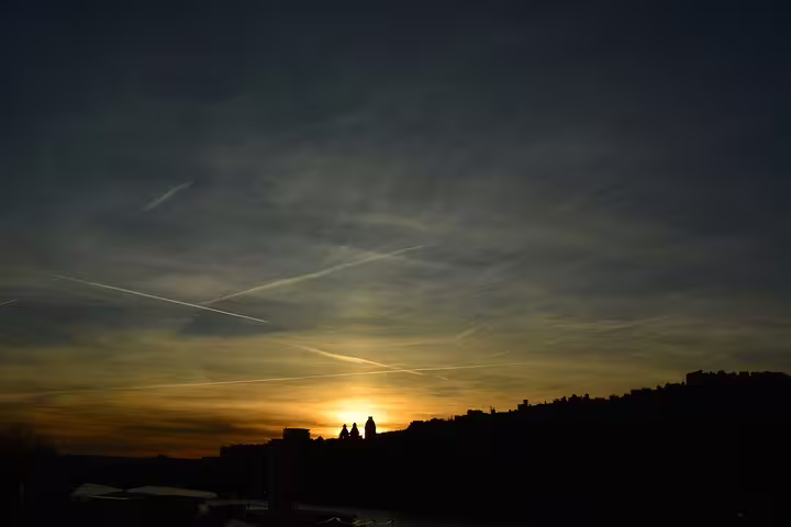 Silhouettes of people watching sunset over Paris skyline with airplane contrails in dramatic sky