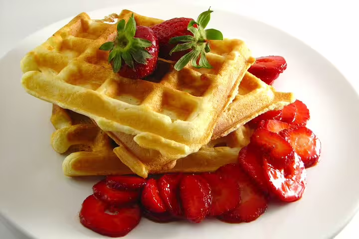 Stack of golden Belgian waffles topped with fresh strawberries and mint leaves on a white plate
