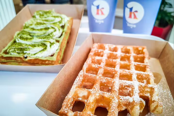 Two waffles in cardboard boxes, one topped with matcha cream swirls, one dusted with powdered sugar, Paris café