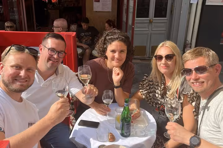 Group of five friends toasting with wine glasses at an outdoor Paris café terrace on a sunny day