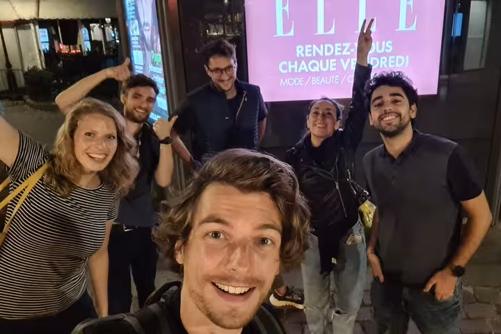 Group of six friends taking a selfie at night in Paris in front of an ELLE magazine billboard