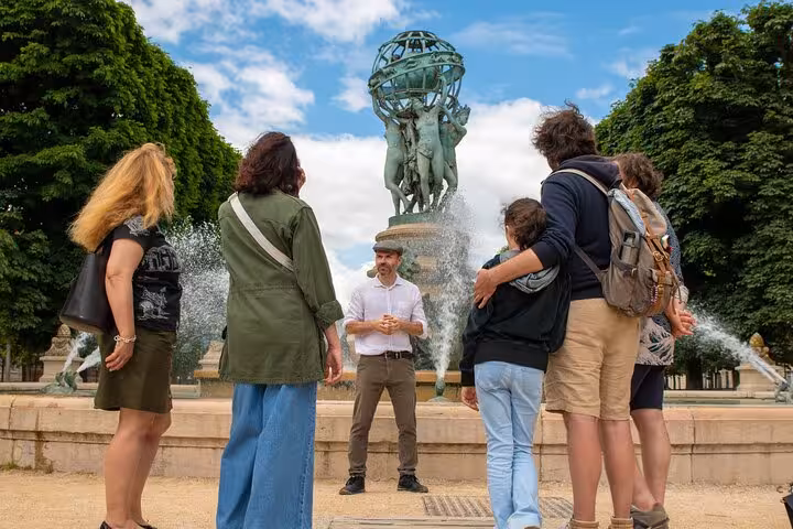Tour guide speaking to group of tourists by ornate fountain in Paris garden