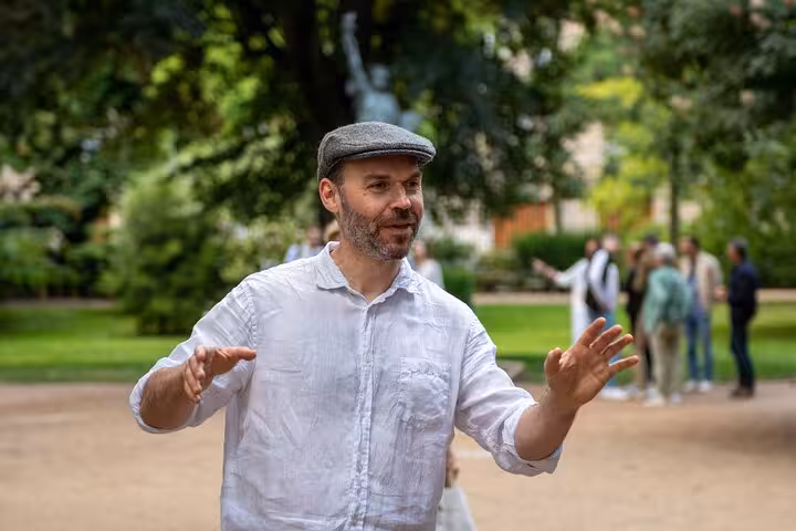 Tour guide gesturing expressively in a Paris park with visitors and statue in background