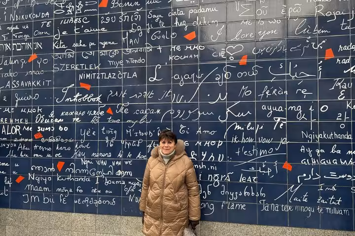 Tourist standing in front of the Wall of Love in Paris covered in multilingual love phrases