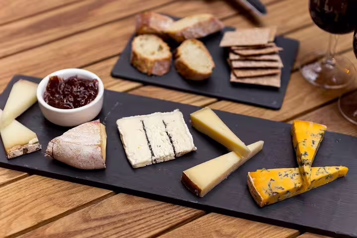 Slate board with assorted French cheeses, jam, crackers, bread, and a glass of red wine