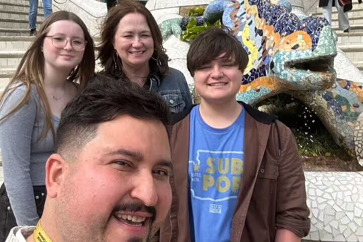 Visitors enjoying a vibrant day at Park Güell in Barcelona, posing with the iconic mosaic dragon sculpture by Gaudí.