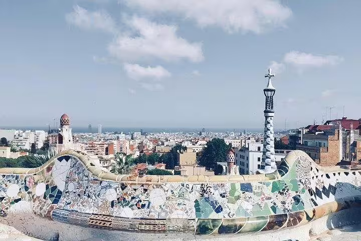 Panoramic view from Park Güell's mosaic terrace overlooking Barcelona's skyline under a blue sky.