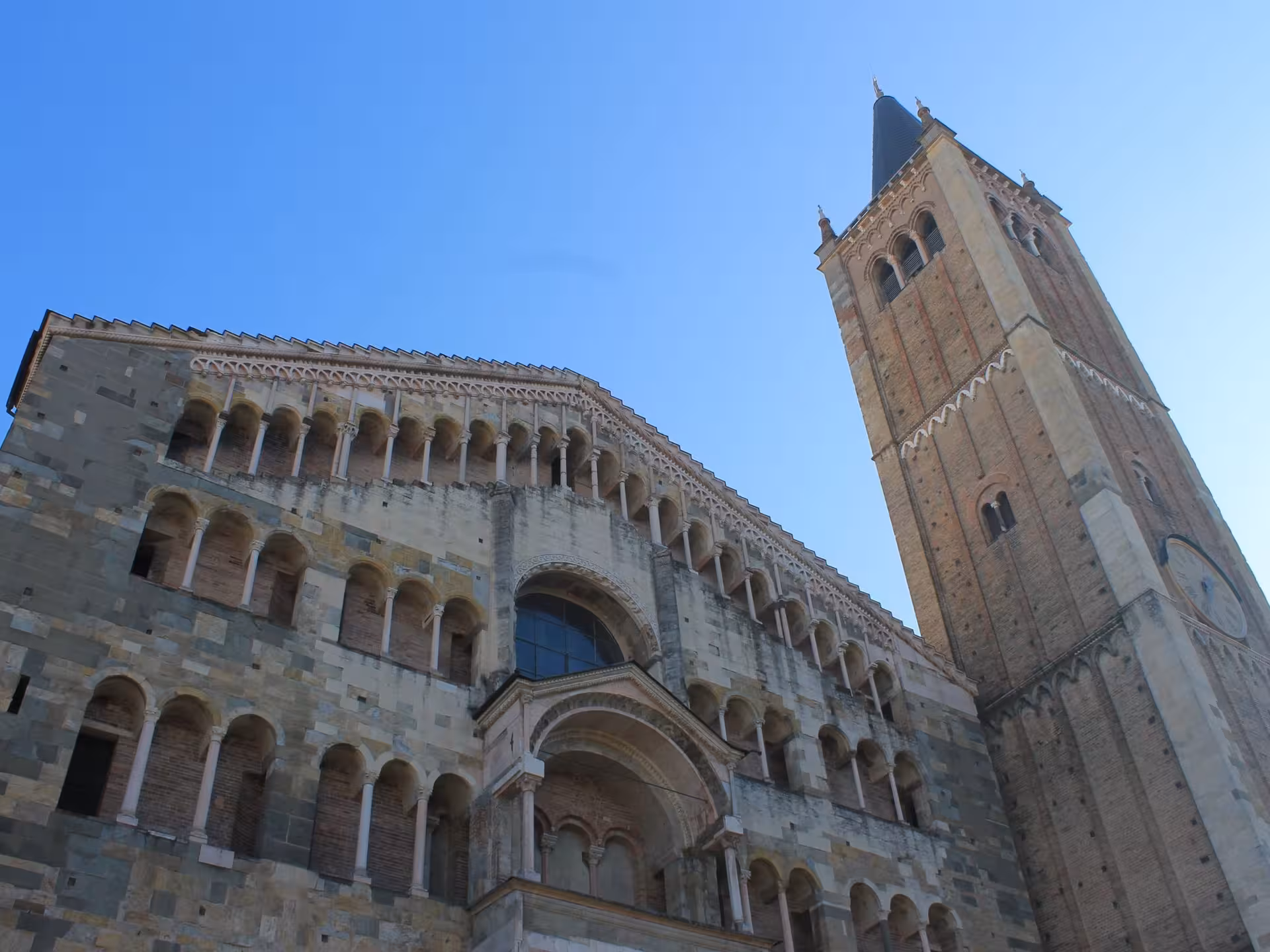 The majestic facade and bell tower of Parma Cathedral under a clear blue sky, a highlight of architectural tours.