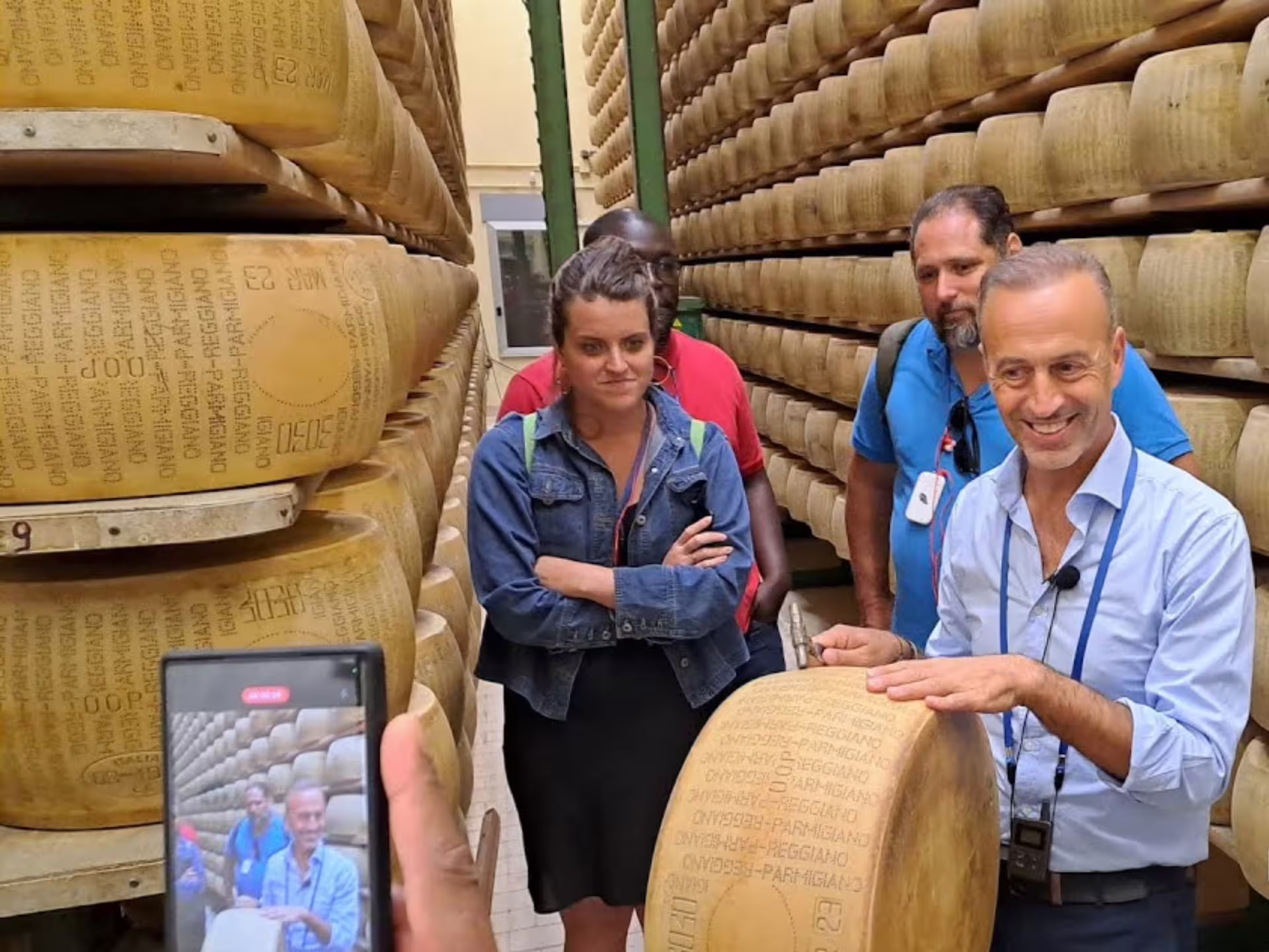Group of tourists learning about Parmesan cheese aging in a factory, surrounded by cheese wheels near Parma.