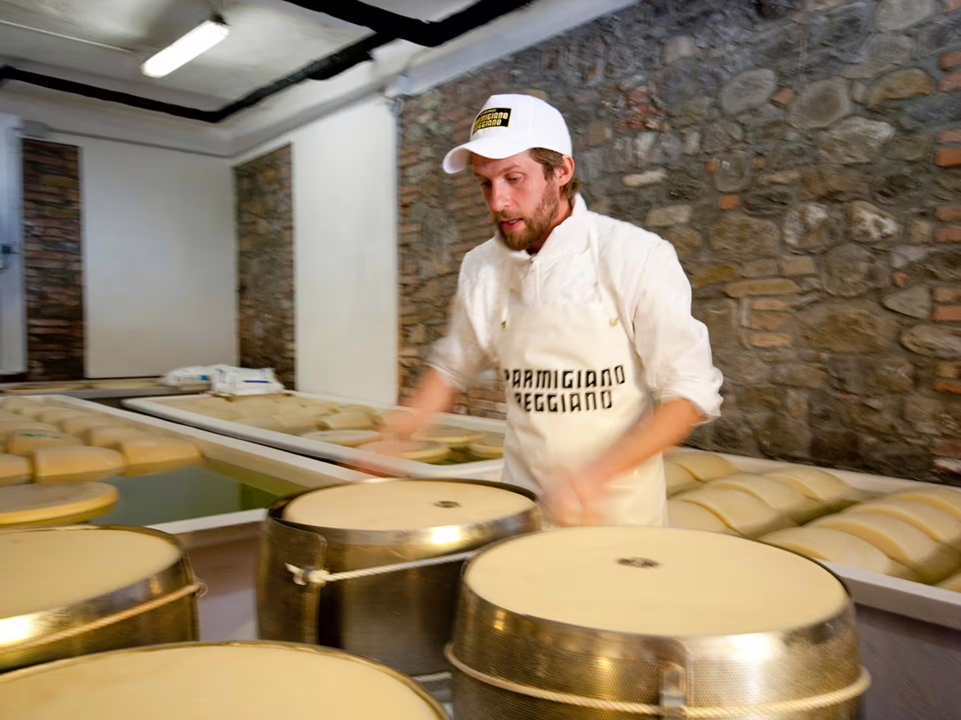 Cheese maker inspects Parmesan wheels during a factory tour near Parma, showcasing authentic cheese production.