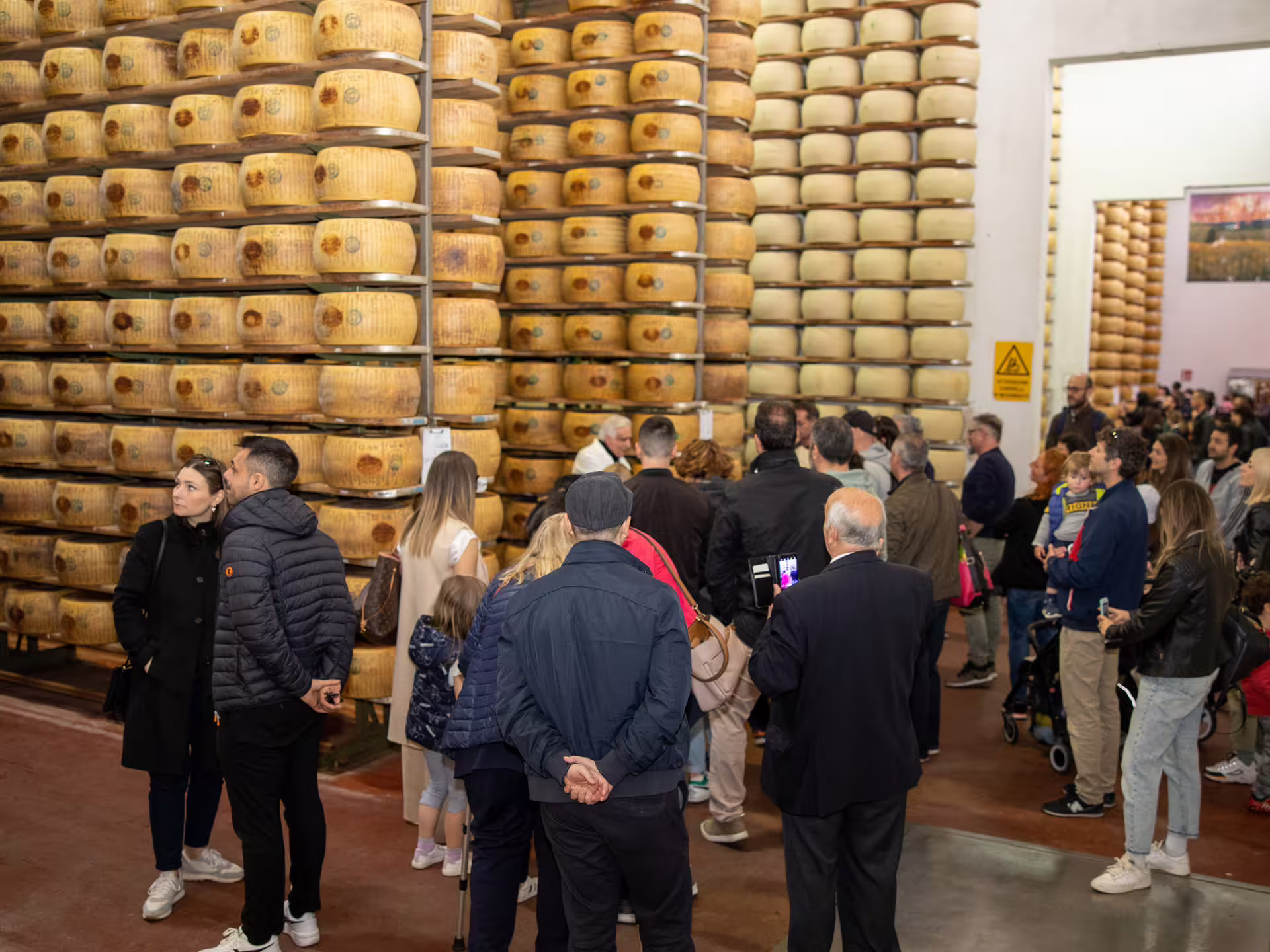 Group tour inside Parmigiano Reggiano warehouse with stacked cheese wheels during Parmesan factory visit near Modena
