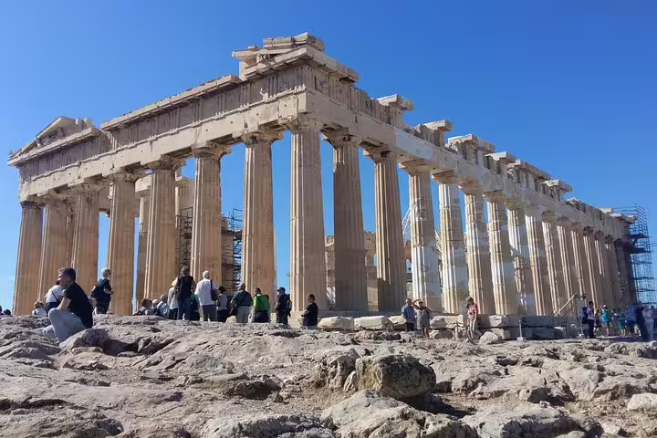Parthenon Temple columns on the Acropolis of Athens, visitors on guided walking tour under clear blue sky