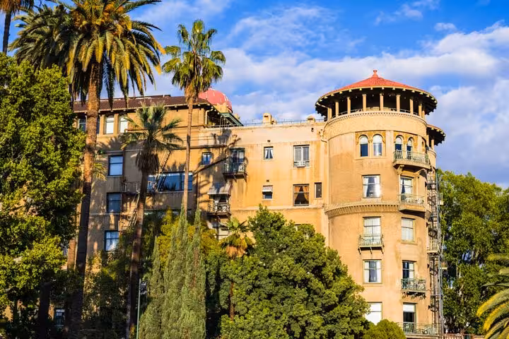 Historic tan building with round tower and red dome surrounded by palm trees in Pasadena