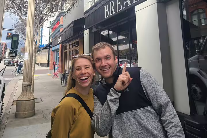 Two smiling people posing on a Pasadena sidewalk outside a restaurant during a walking tour