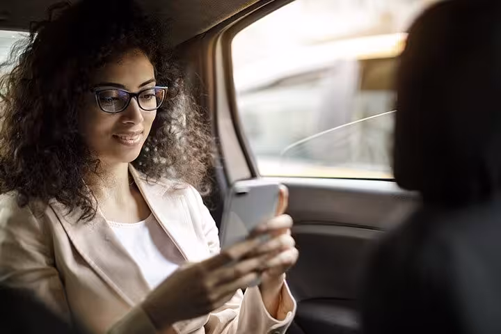 Woman smiling at phone in backseat of private transfer car