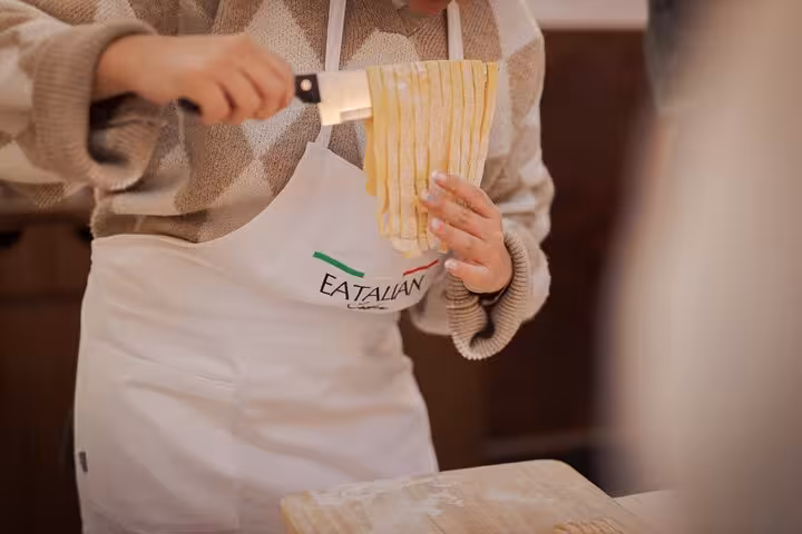Close-up of a participant cutting pasta dough during a cooking class in Rome, Piazza Navona, highlighting hands-on learning.