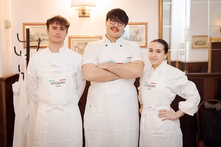 Three chefs in white aprons pose at a pasta and tiramisu cooking class in Rome, Piazza Navona.