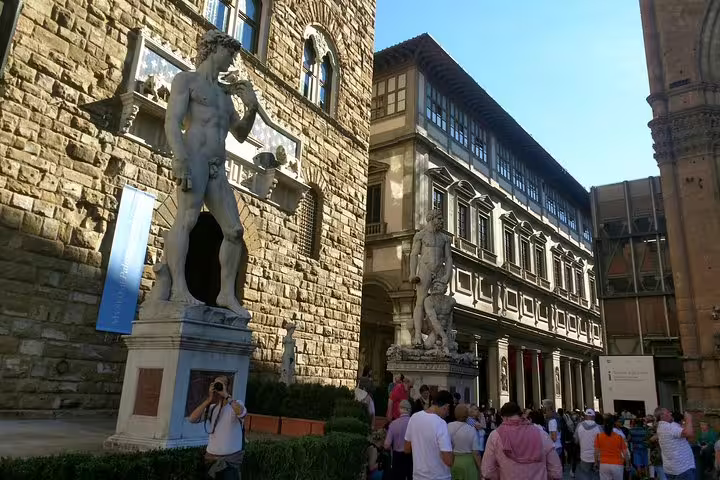 Tourists gather near David statue replica at Piazza della Signoria, Florence, with Uffizi Gallery in background