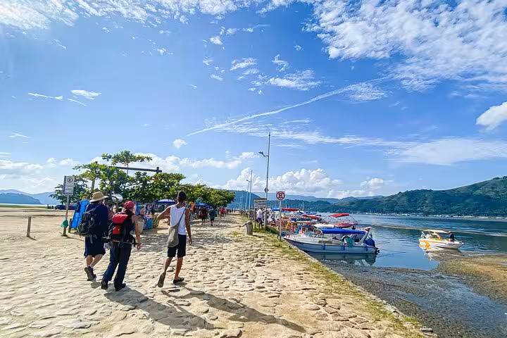 Tourists stroll along a scenic waterfront path near boats at Peak Sugar Bread adventure site under a vibrant sky.
